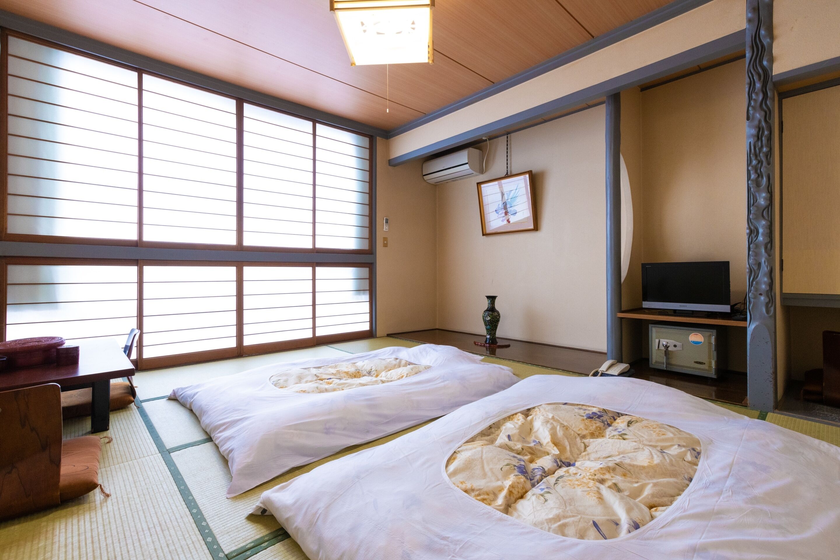Une pièce de style japonais traditionnel, avec un sol recouvert de tatamis, deux nattes de tatami, un bureau en bois, une télévision et une porte coulissante.