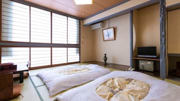 Une pièce de style japonais traditionnel, avec un sol recouvert de tatamis, deux nattes de tatami, un bureau en bois, une télévision et une porte coulissante.