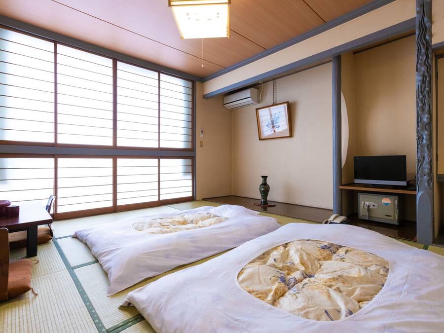 Une pièce de style japonais traditionnel, avec un sol recouvert de tatamis, deux nattes de tatami, un bureau en bois, une télévision et une porte coulissante.