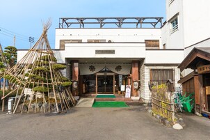 Edificio tradizionale giapponese con struttura in legno all'esterno, un tappeto verde e un cartello sopra l'ingresso.
