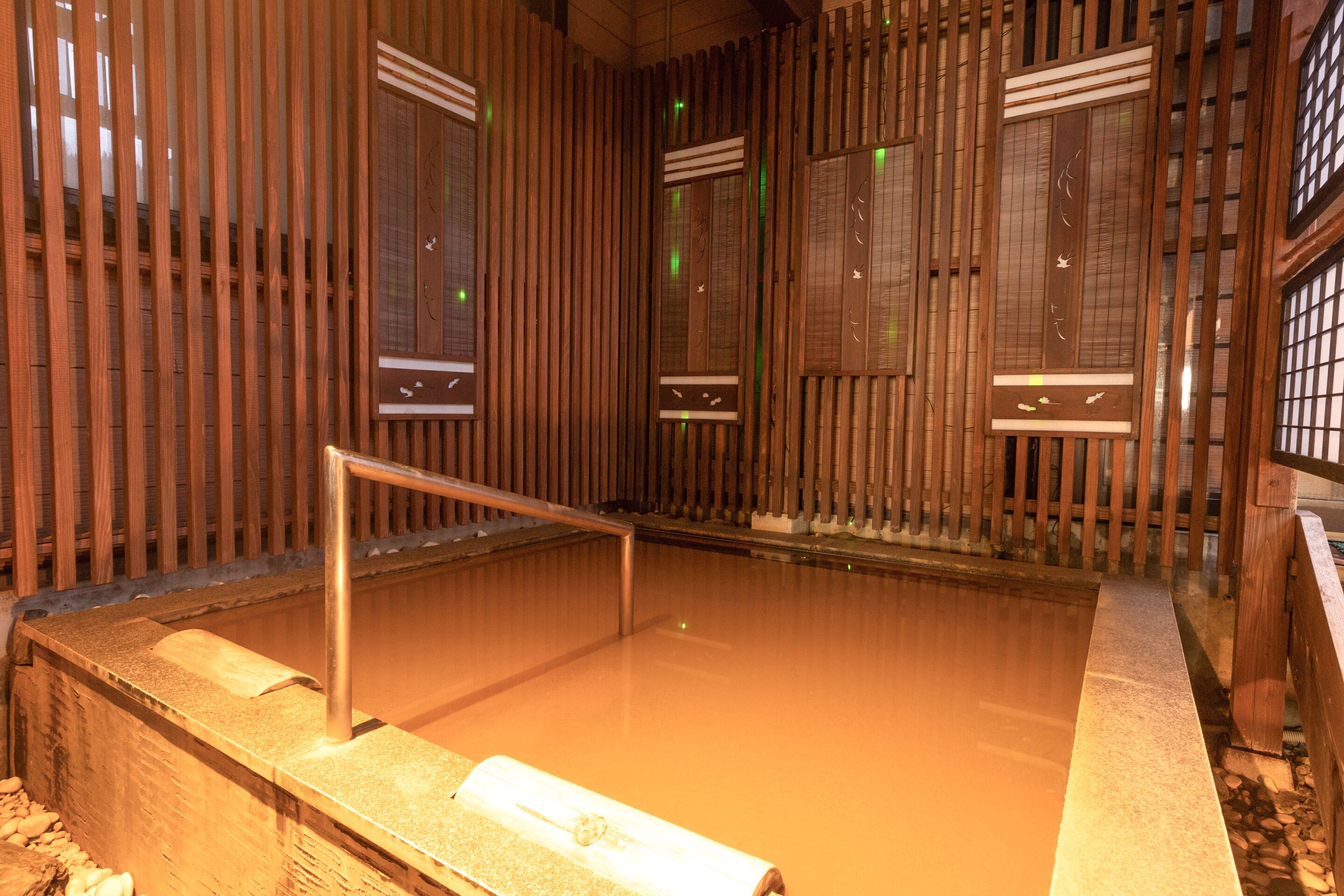 A traditional Japanese onsen with wooden sliding doors and a wooden deck leading into the hot spring.