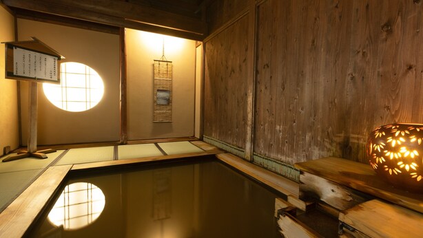 A traditional Japanese onsen with a wooden interior, a tatami mat floor, a wooden bench, and a lantern.
