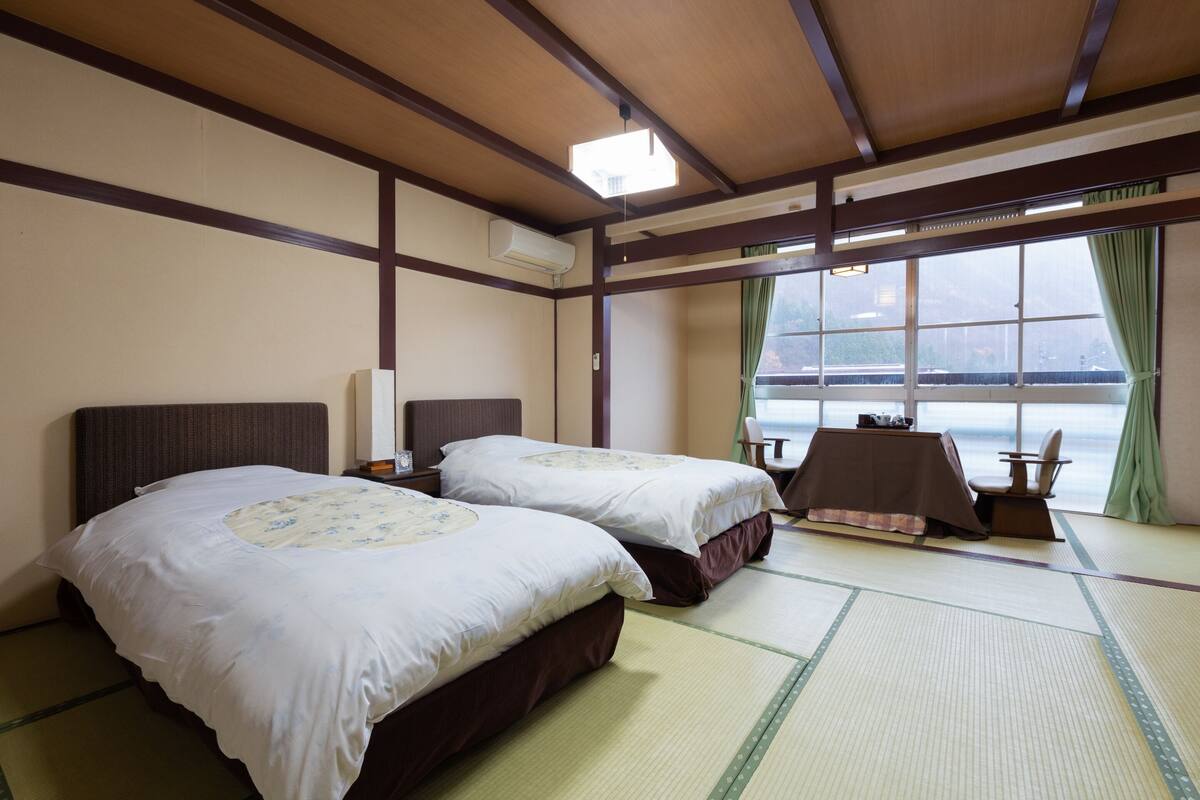 A hotel room with two beds, a table, and a view of the sea.