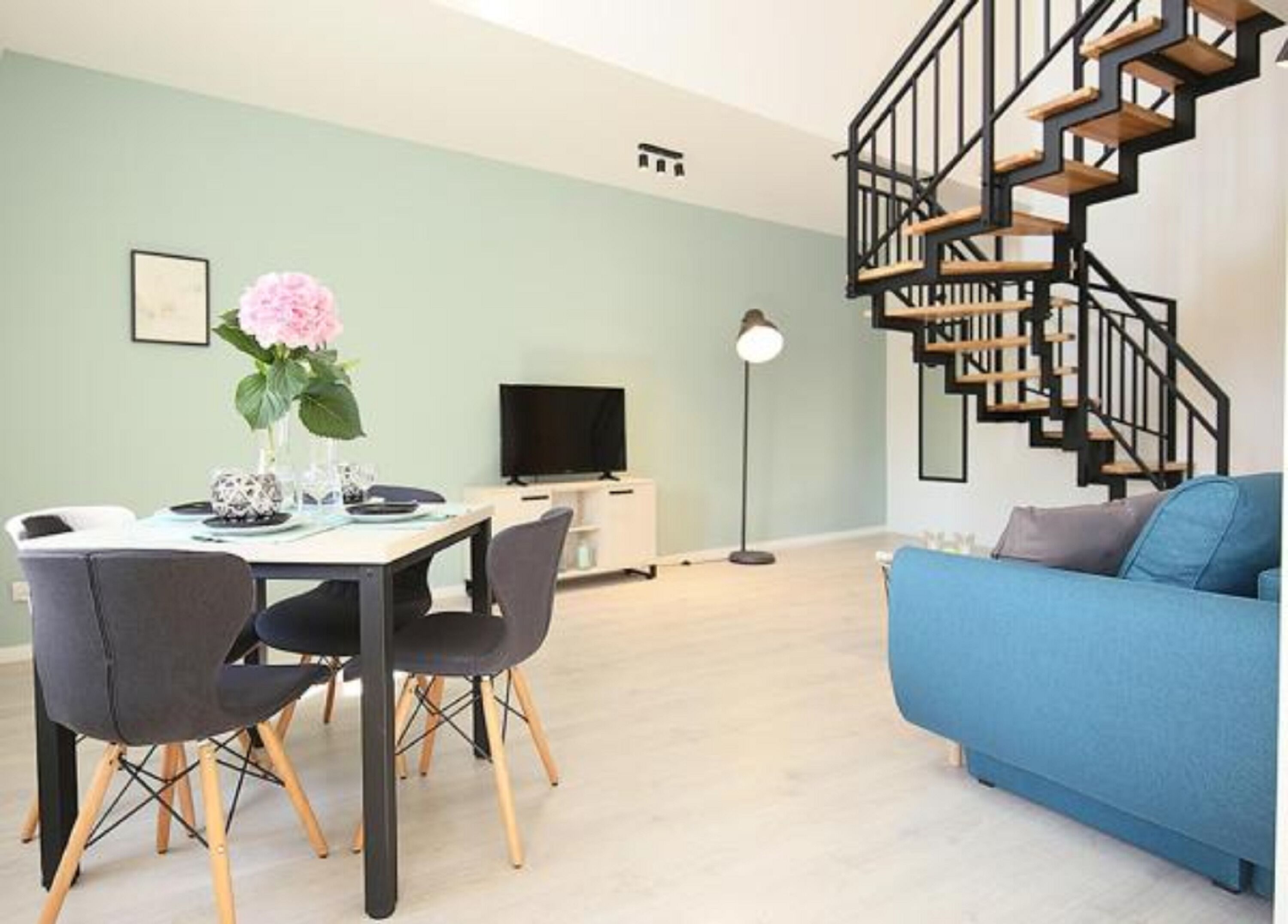 A modern living room with a blue sofa, a dining table with chairs, a TV, and a staircase.