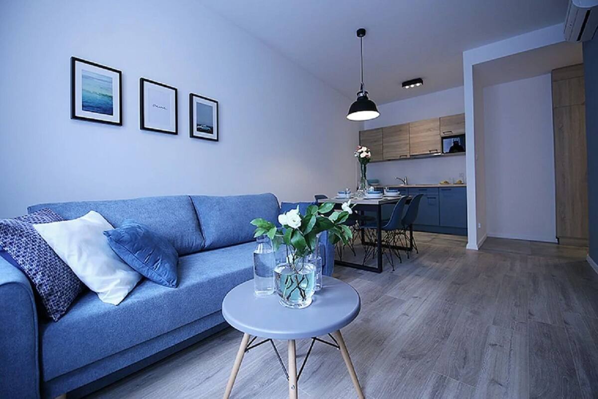 A modern living room with a blue sofa, a round table with vases, and framed pictures on the wall.