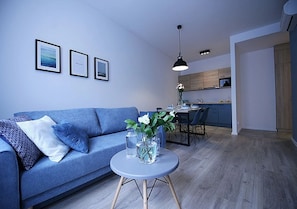 A modern living room with a blue sofa, a round table with vases, and framed pictures on the wall. - Absyntapart -  Stare Miasto (Wroclaw)