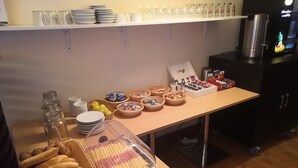 Une table de buffet proposant divers aliments, notamment du pain, des pâtisseries et des boissons.