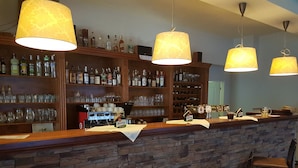 Un espace bar doté d’un comptoir en pierre, de plusieurs étagères remplies de bouteilles d’alcool et de lampes suspendues.