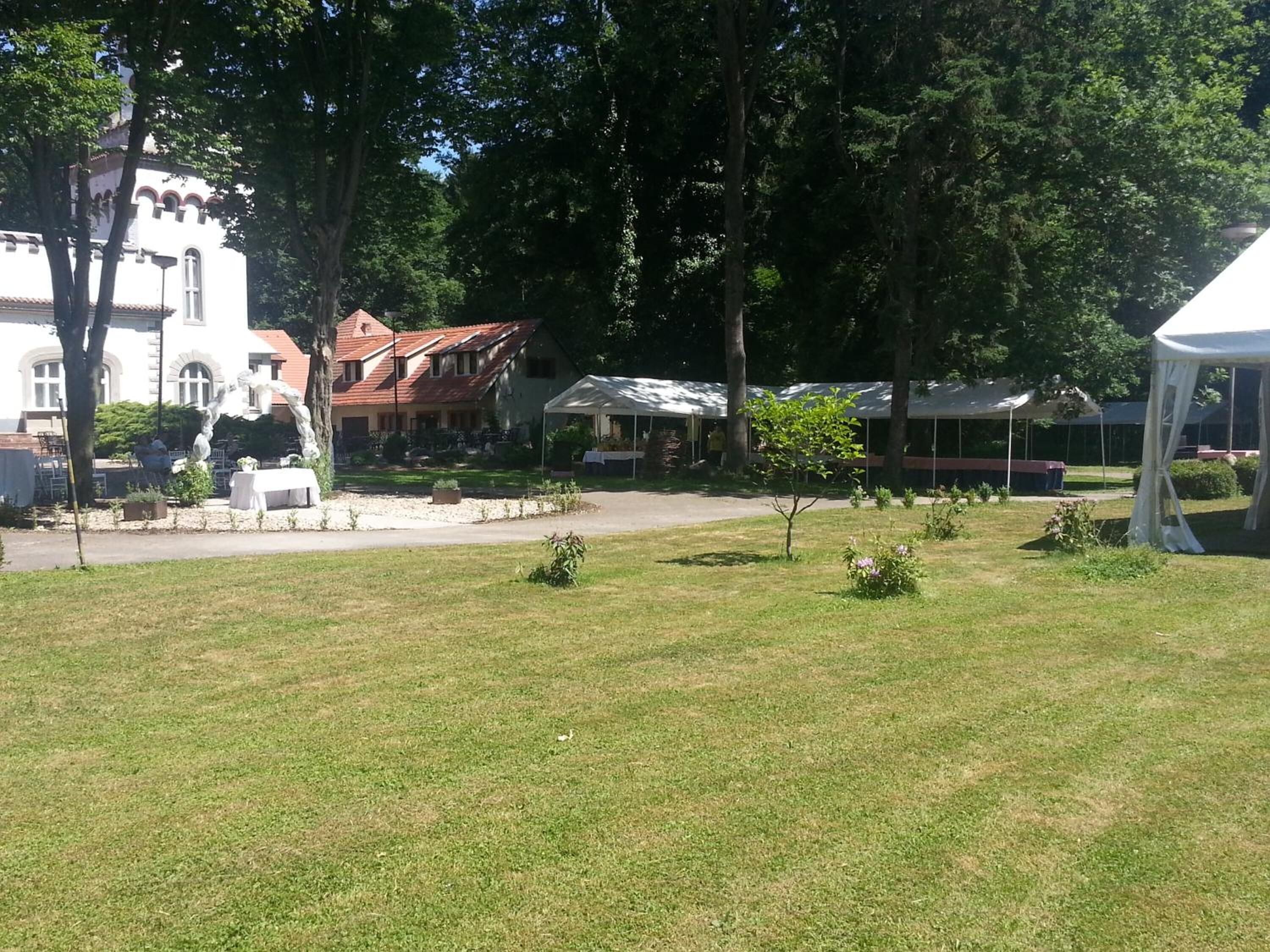 A grassy outdoor area with a white tent, a building with a red roof, and trees.