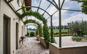 A covered outdoor corridor with a brick floor, potted plants, and a view of a vineyard in the distance. - Prime Alture Wine Resort (Casteggio)