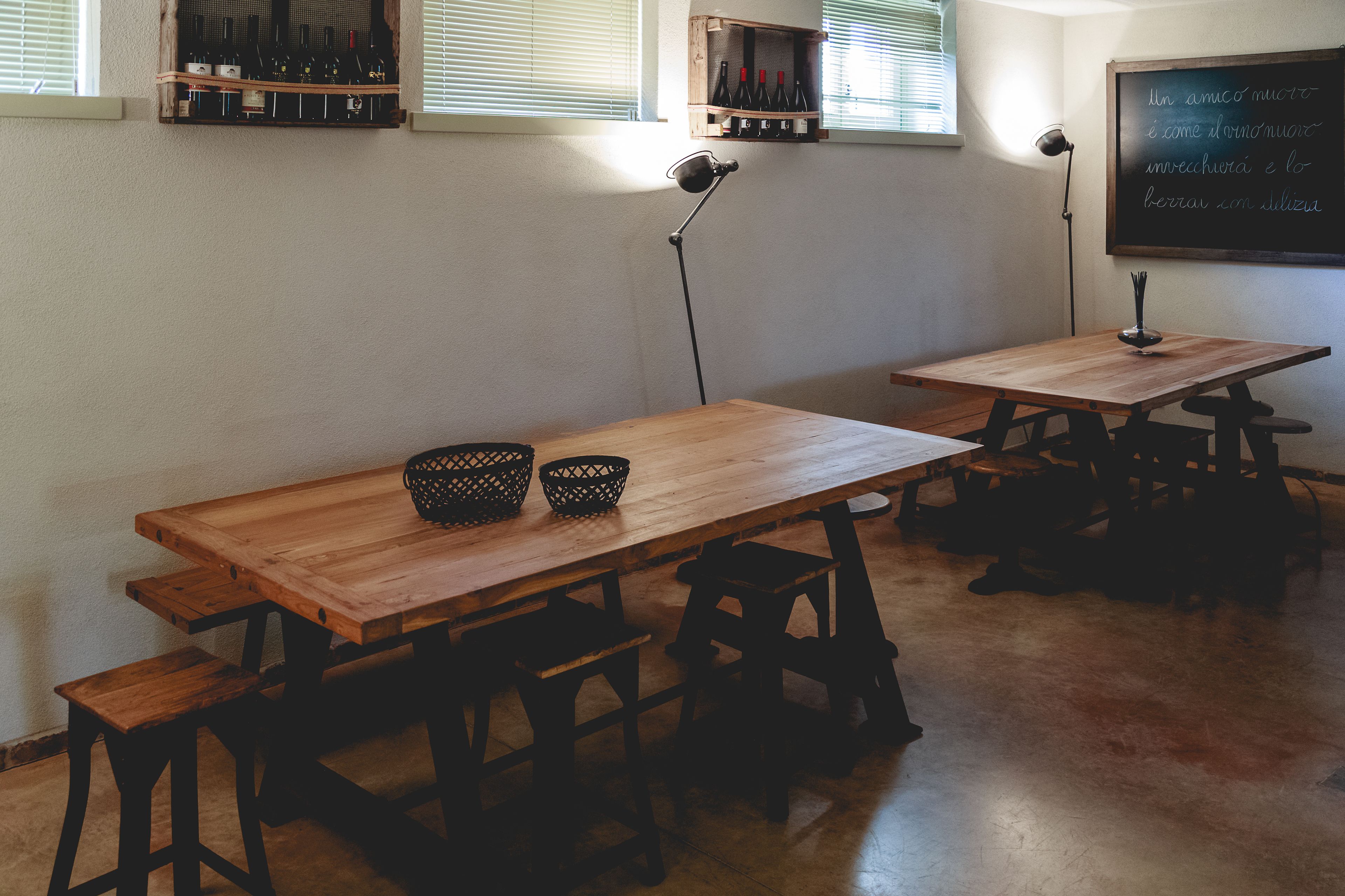 Une salle de classe avec des tables et des bancs en bois, un tableau noir et des bouteilles de vin disposées sur des étagères.