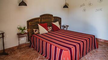 Una camera da letto con una testiera in legno, una coperta a righe, un comodino con un vaso di fiori e una parete con scritte decorative.