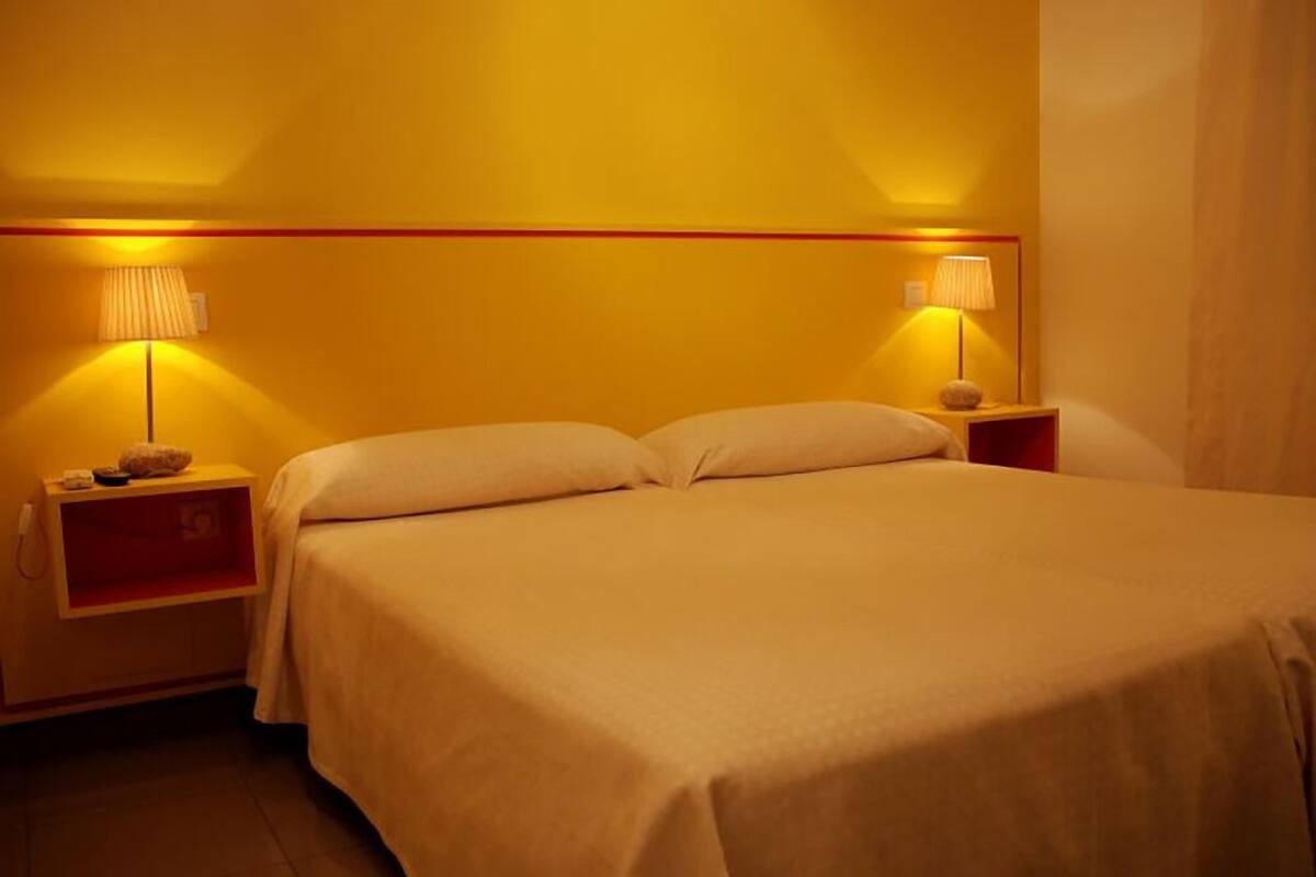 Une chambre d’hôtel avec un grand lit, deux tables de chevet avec des lampes et un détail rouge sur la tête de lit.