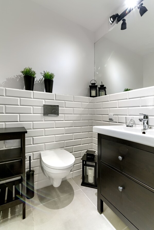 A modern bathroom with white subway tiles, a white toilet, a dark wooden vanity, and a small black lantern on the floor. - Dream Holiday - Apartament Bastion Wałowa (Gdansk)