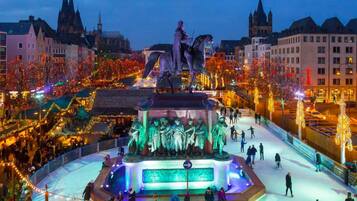 A public square with a central fountain, surrounded by buildings and festive lights.