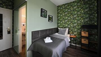 A bedroom with a bed, a nightstand, a wall with a leafy pattern, and a door leading to a bathroom.