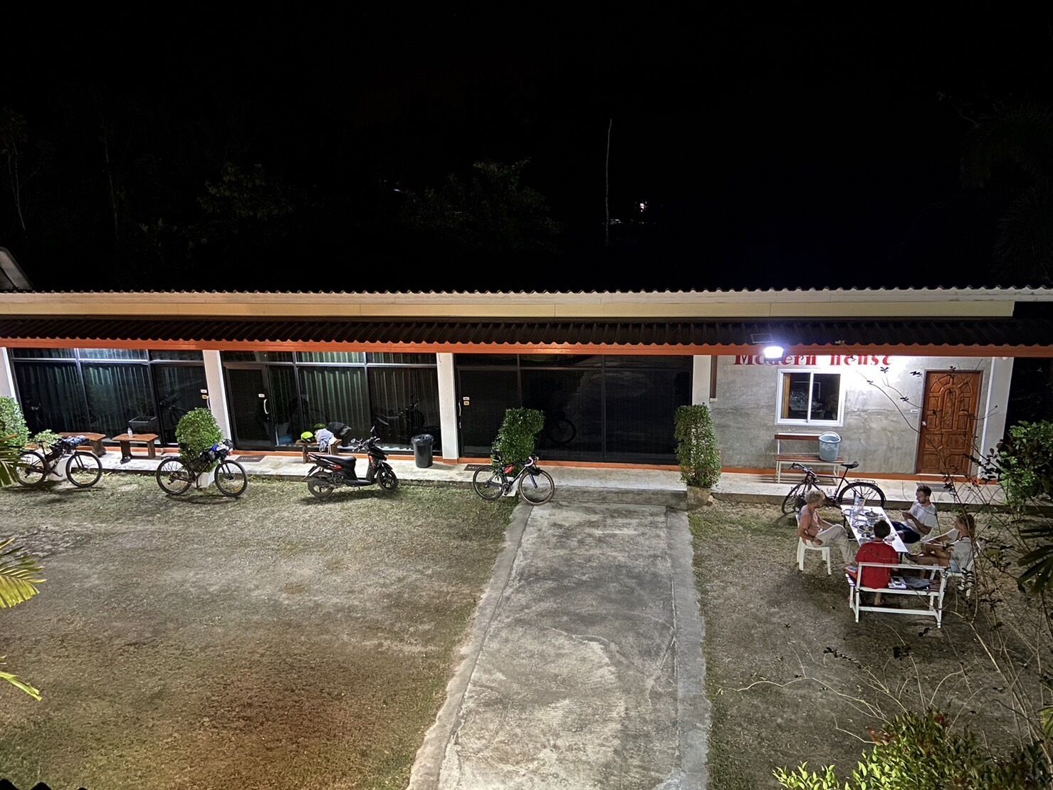 A building with a tiled roof and a covered outdoor area. There are bicycles parked in front and a few people sitting outside.