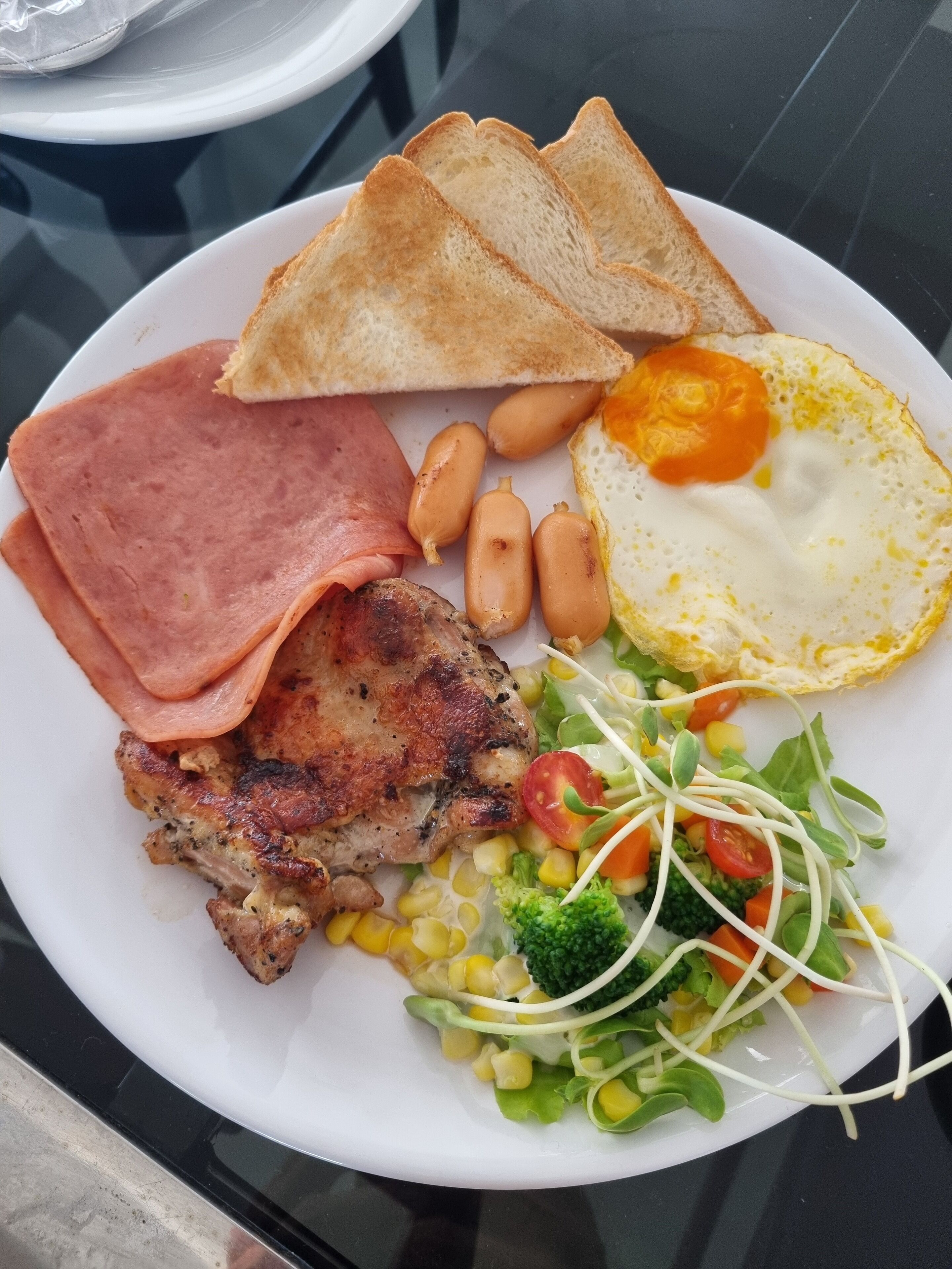 A plate of food including toast, eggs, ham, sausages, and vegetables.