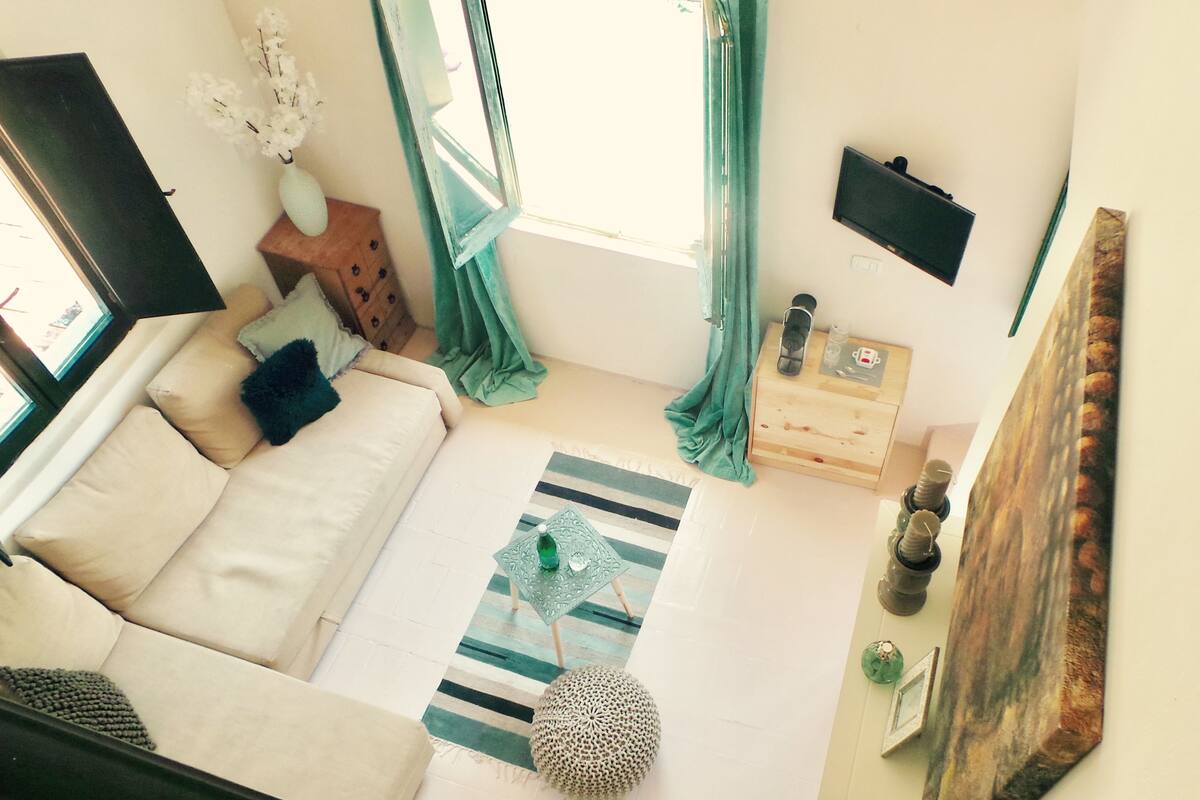 A living room with a sofa, a wooden side table, a striped rug, and a painting on the wall.