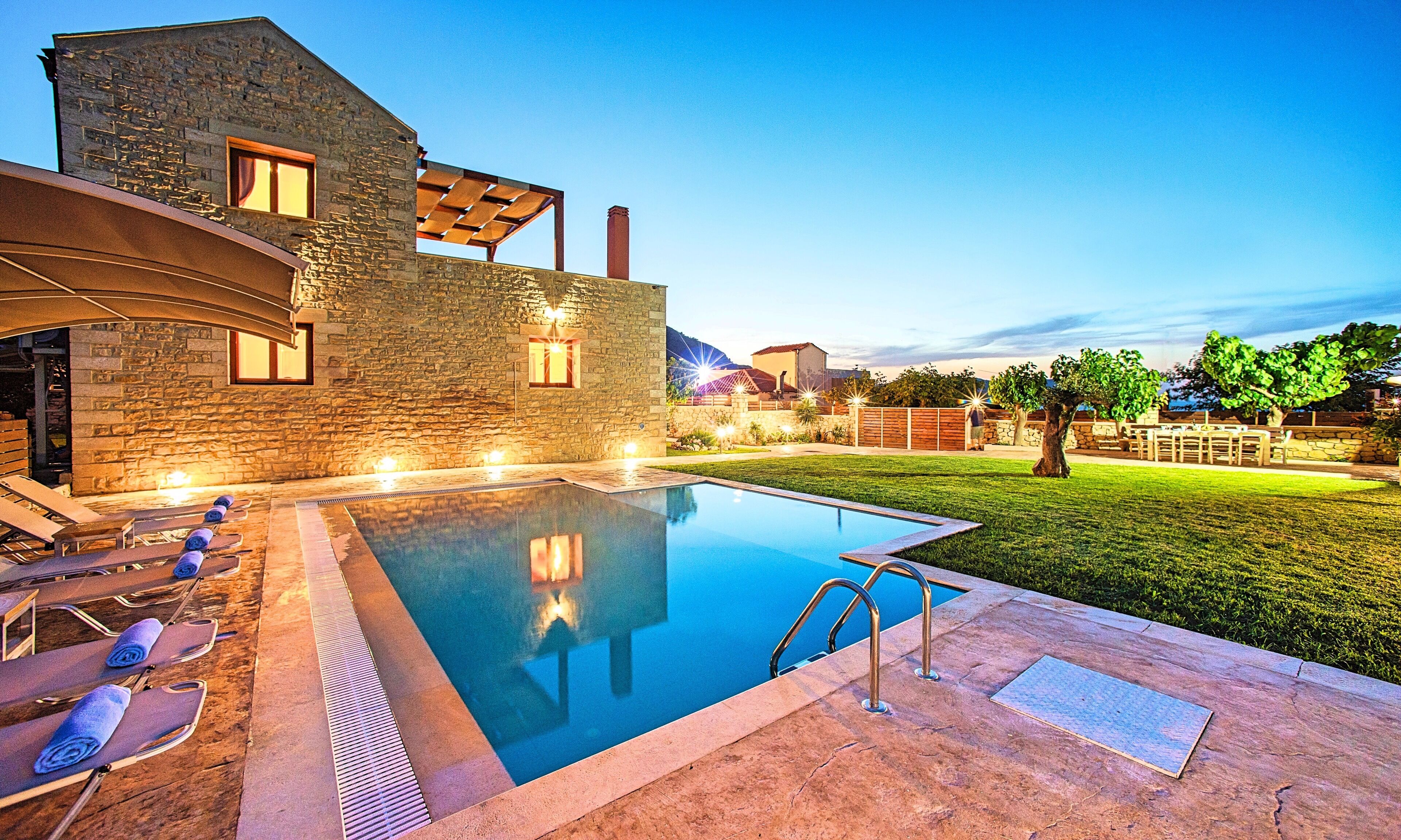 A modern pool area with stone walls, lounge chairs, and a well-lit patio.