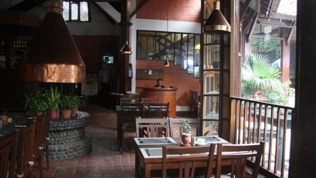 A cozy restaurant with brick walls, wooden furniture, and a large copper chimney. - Mandap Hotel (Kathmandu)