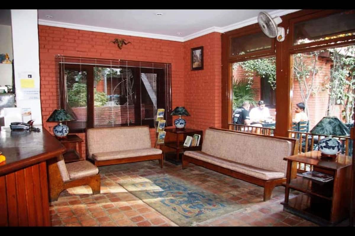 A room with a brick wall, a wooden bench, a small table, and a fan.