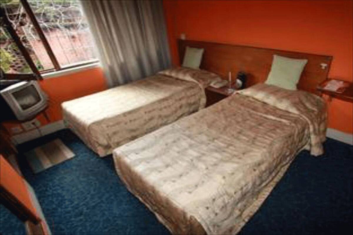 A hotel room with two beds, a television, and a window with curtains.