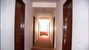 A hallway with wooden doors on either side, leading to a room with a red carpet and a visible window. - Mandap Hotel (Kathmandu)