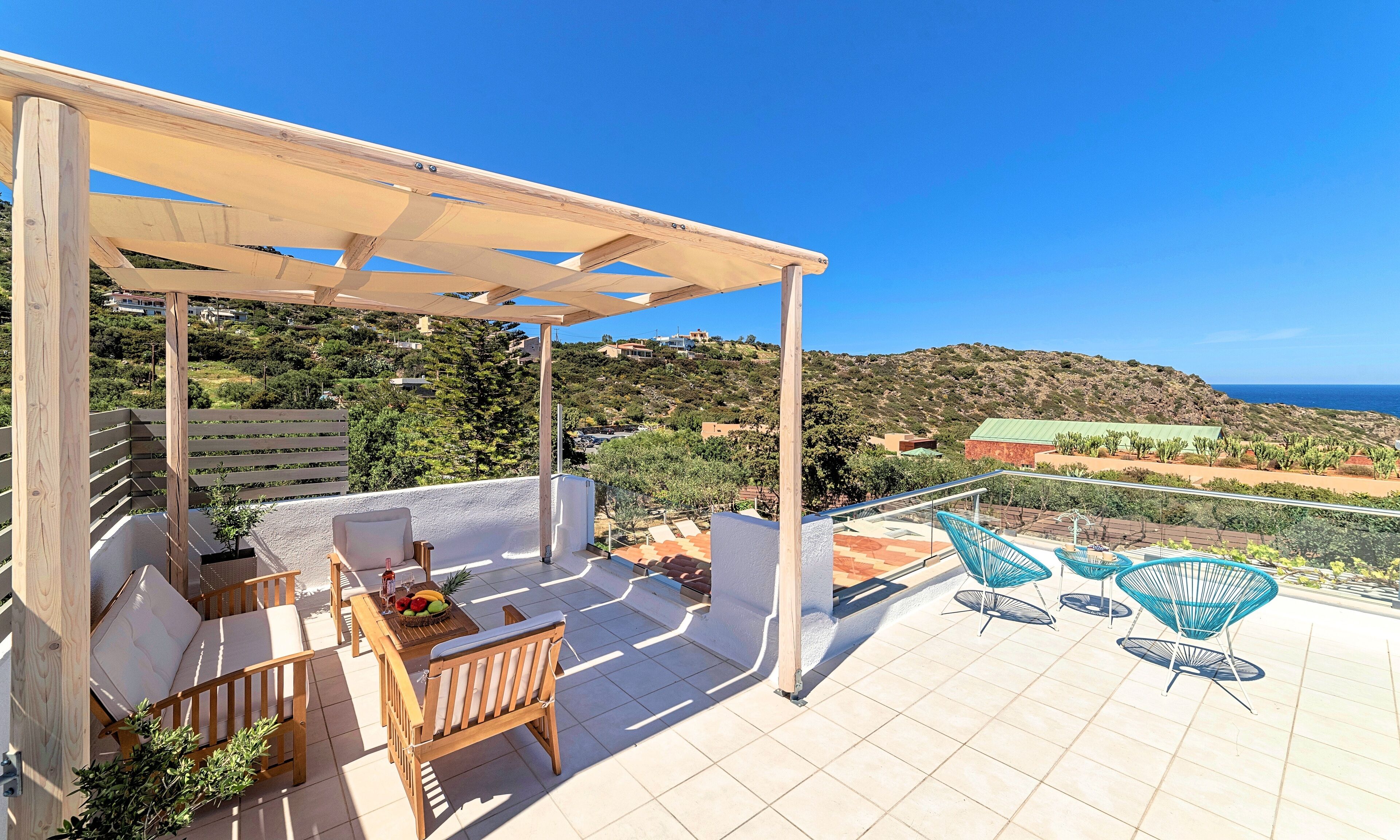 A terrace with a wooden pergola, outdoor seating, and a view of the sea and hills.