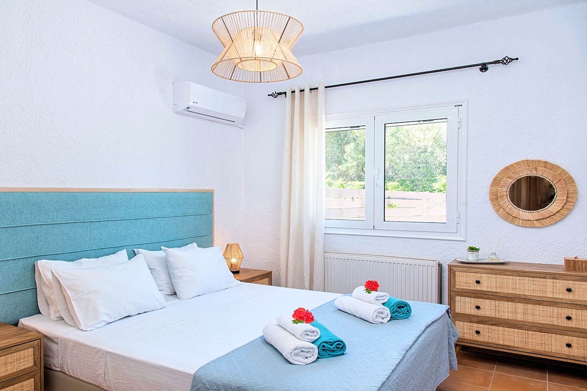 Un dormitorio con cama, mesitas de noche, ventana, aire acondicionado montado en la pared, lámpara colgante y espejo.