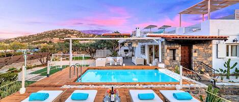 A poolside area with lounge chairs, a barbecue, and a view of a hillside.