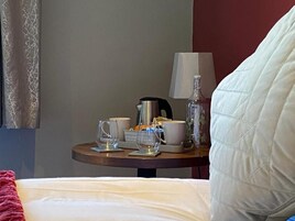 Una habitación de hotel con cama, una mesita de noche con lámpara, una botella y una taza.