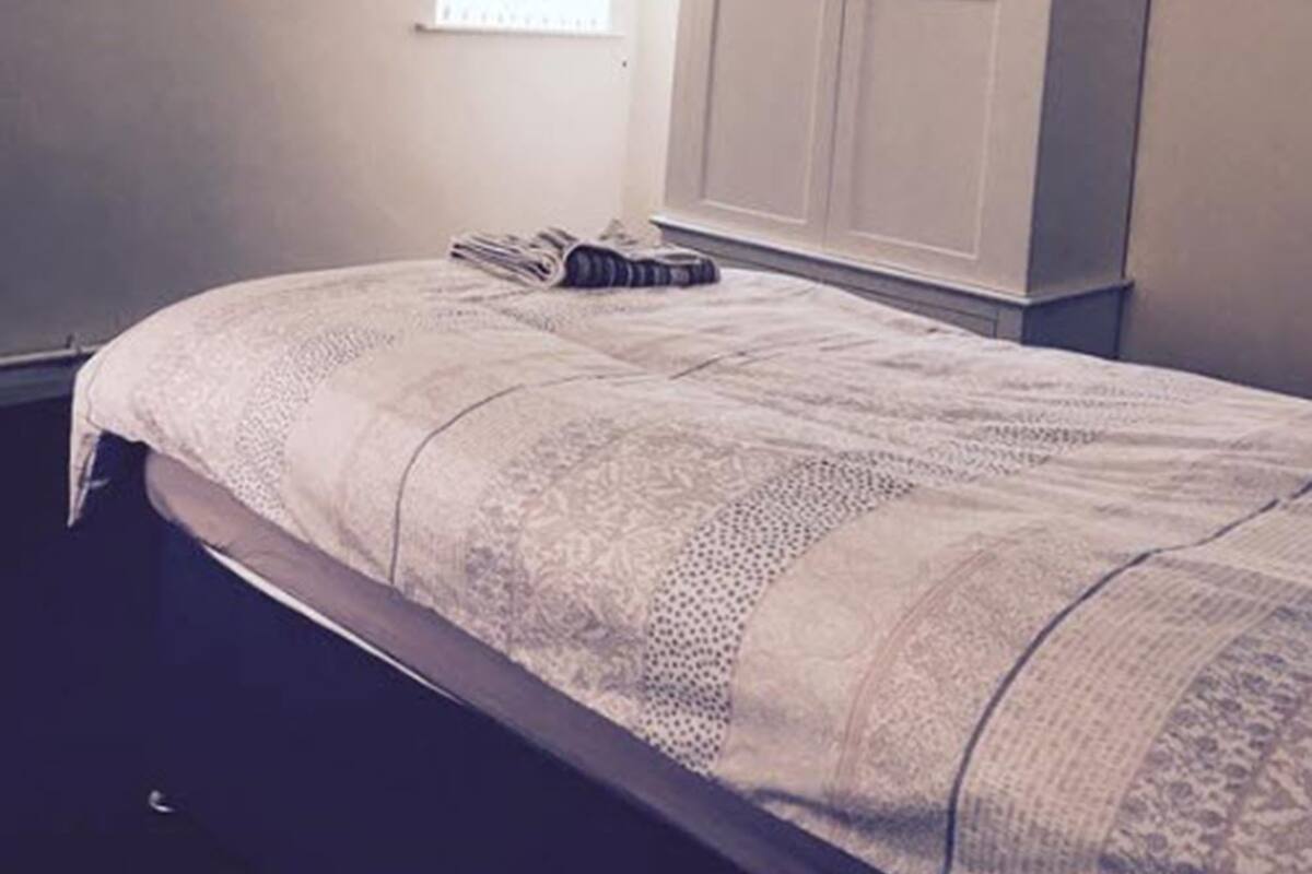 Quarto com cama, guarda-roupa, televisão na parede e janela com persianas.