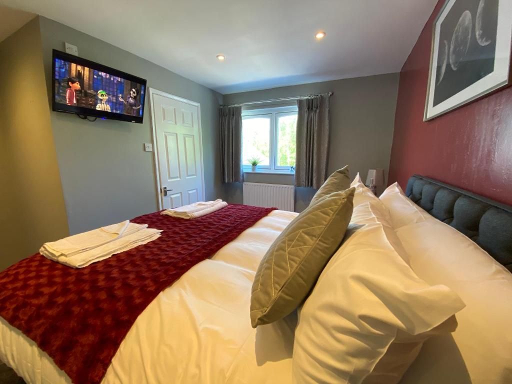 A hotel room with a bed, a television on the wall, a window with curtains, and a radiator.