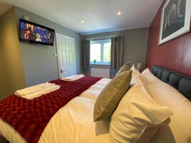 Una habitación de hotel con cama, televisión en la pared, ventana con cortinas y radiador.