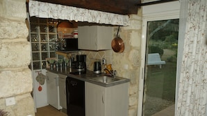 A compact kitchen with a built-in dishwasher, a coffee maker, and a hanging pot. - Chambres d'hôtes Sous les Chênes (Lussan)