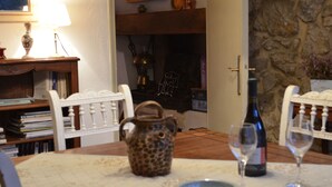 A dining table with a pitcher, wine bottle, and glasses, surrounded by chairs and a bookshelf. - Chambres d'hôtes Sous les Chênes (Lussan)