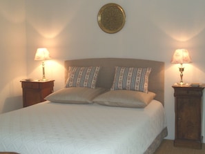Een netjes opgemaakt bed met een gekleurd kussen, twee nachtkastjes met lampen en een decoratief bord aan de muur.