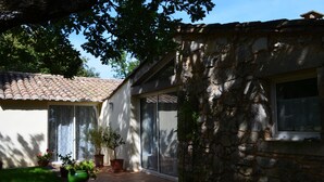 A stone house with a tiled roof, a glass door, and a small window. - Chambres d'hôtes Sous les Chênes (Lussan)