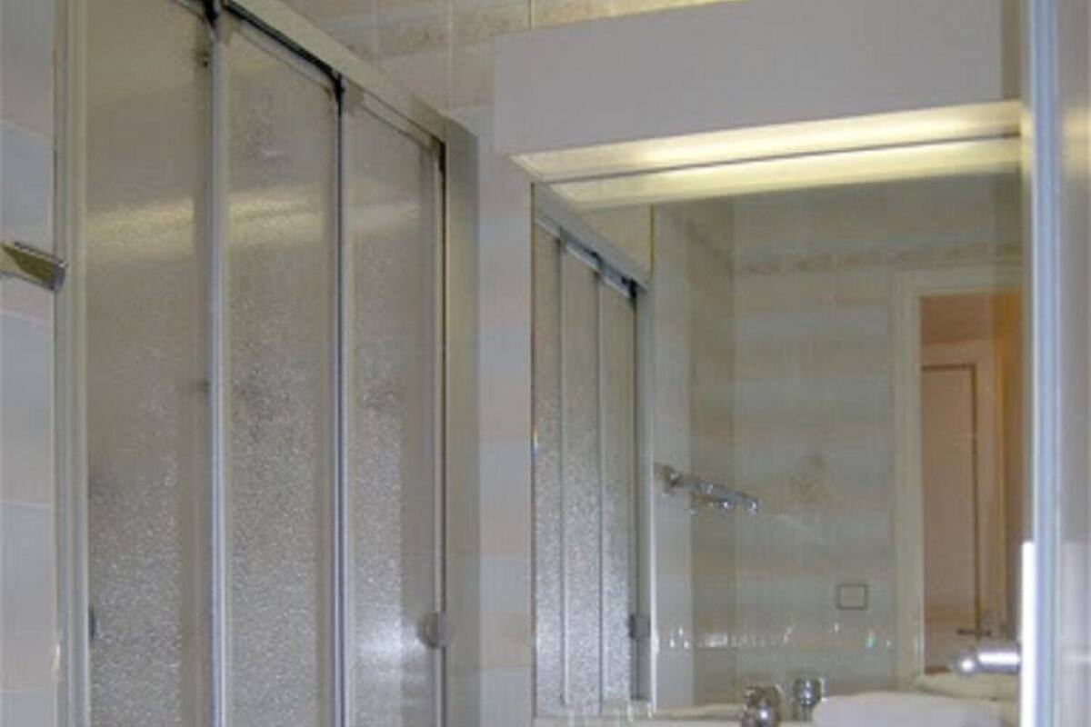 A bathroom with a glass shower enclosure, a white sink with a mirror above it, and a tiled floor.