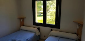 Ein kleines Zimmer mit einem Bett, einem Fenster mit Blick auf Grünflächen und einem schlichten Holzregal.