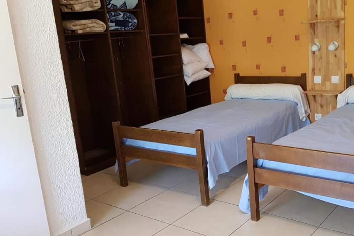 A room with two wooden beds, a wardrobe, and a tiled floor.