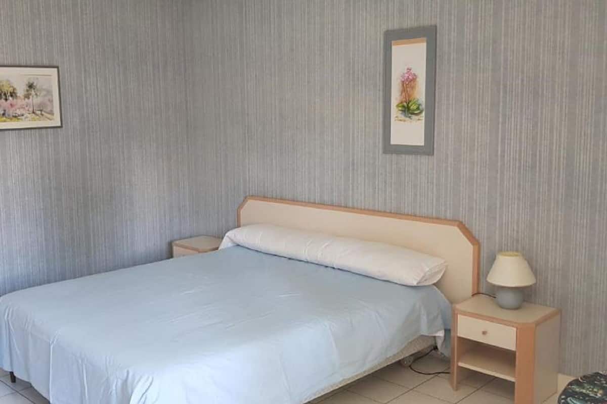 A bedroom with a single bed, a nightstand with a lamp, and two framed pictures on the wall.