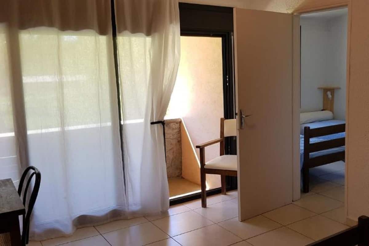 A bedroom with a bed, a chair, a desk, and a window with curtains.