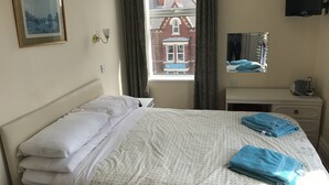 A hotel room with a bed, a bedside table, a TV, and a window with curtains. - Viking Guest House (Bridlington)