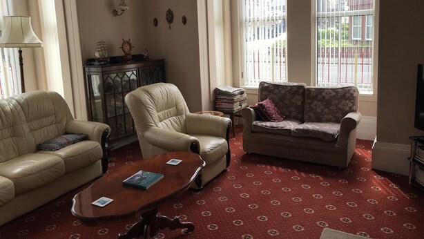 A living room with a beige sofa, a floral-patterned sofa, a wooden coffee table, and a patterned carpet. - Viking Guest House (Bridlington)