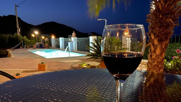 A glass of red wine on a table with a pool and mountains in the background. - Casa Rural Mi Abuela María - Adults Only (Mojacar)