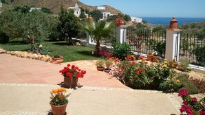 A garden with potted plants and flowers, a white building, and a view of the sea and hills. - Casa Rural Mi Abuela María - Adults Only (Mojacar)