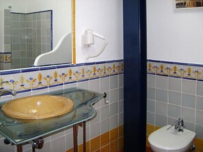 Une salle de bain avec un lavabo en verre, un lavabo sur colonne blanc et un miroir.