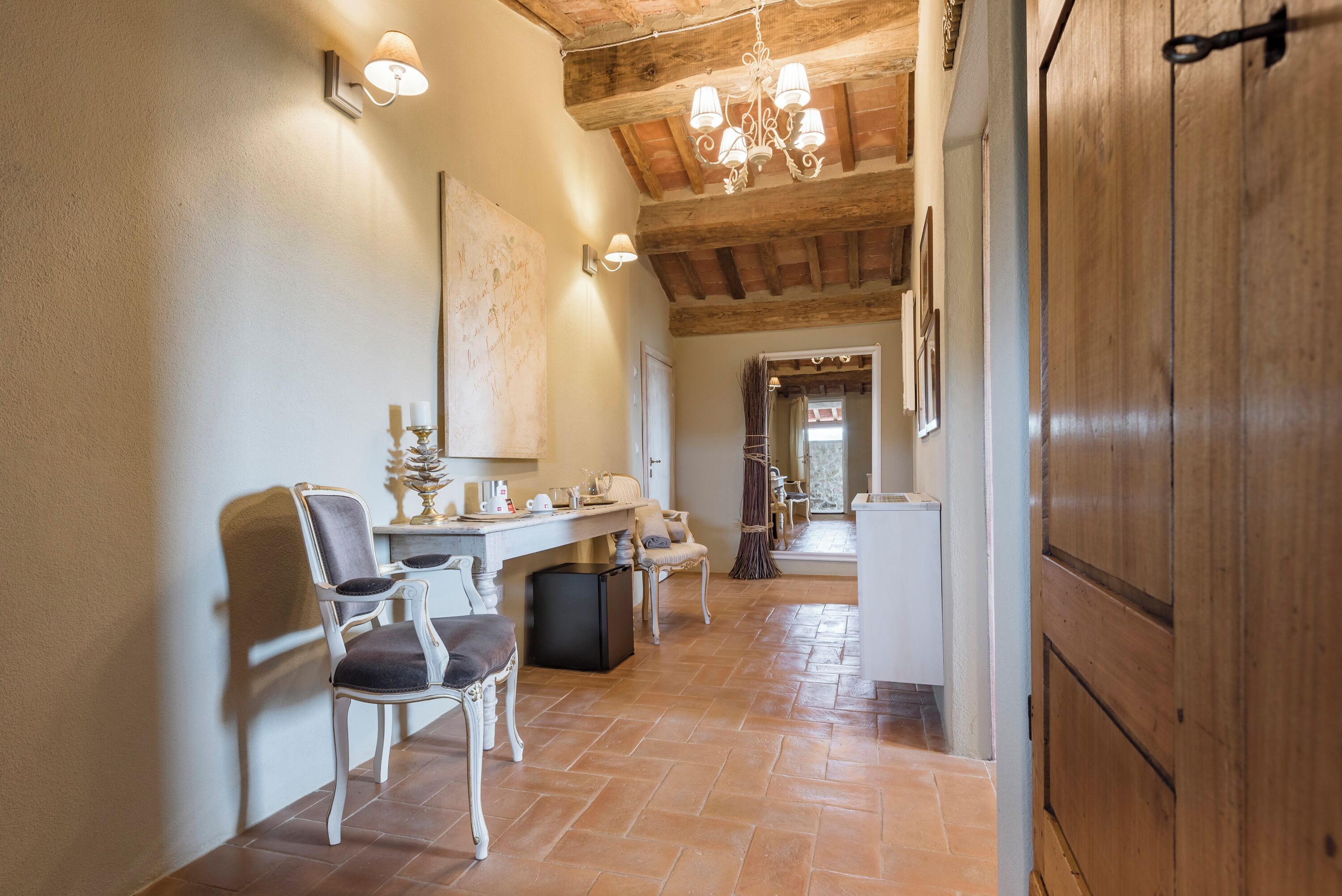 A hallway with a wooden ceiling, a dining area with chairs and a table, and a door on the right.